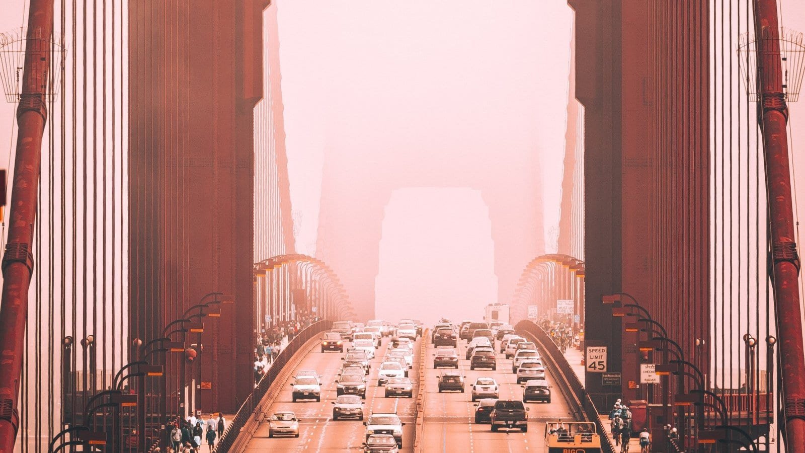 Puente en penumbra con tráfico avanzando hacia la niebla, en tonos rojizos